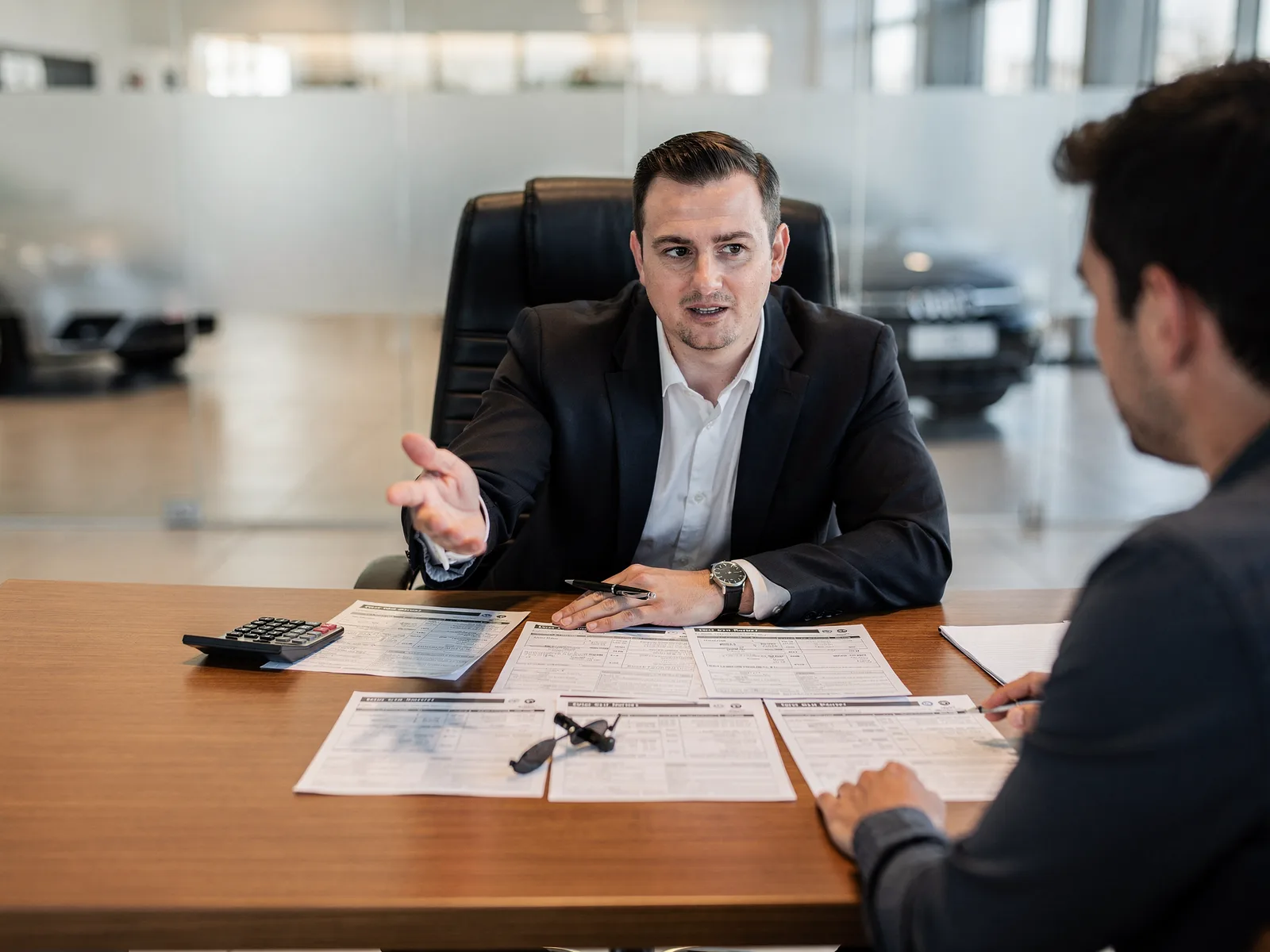 Finance manager at a dealership desk talking a customer through printed payment options