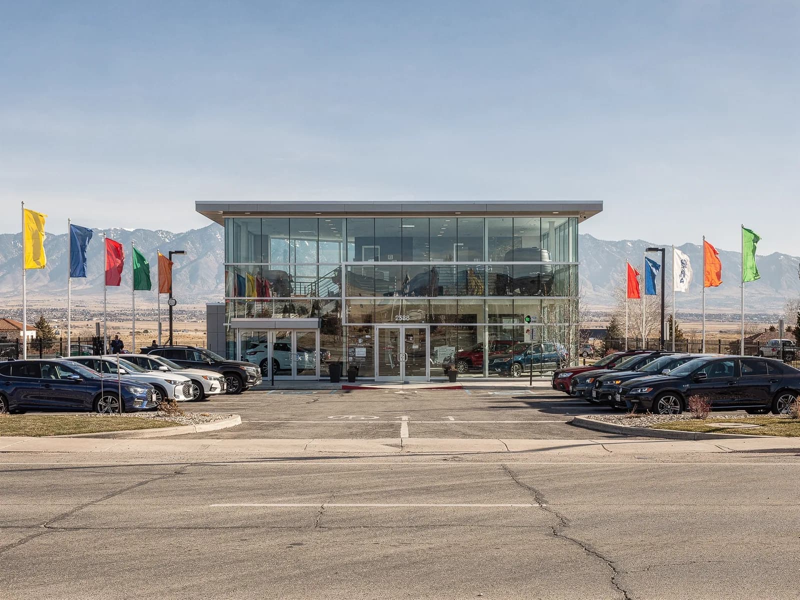 Street view of a single-site car dealership with a glass showroom, flags and the Front Range on the horizon