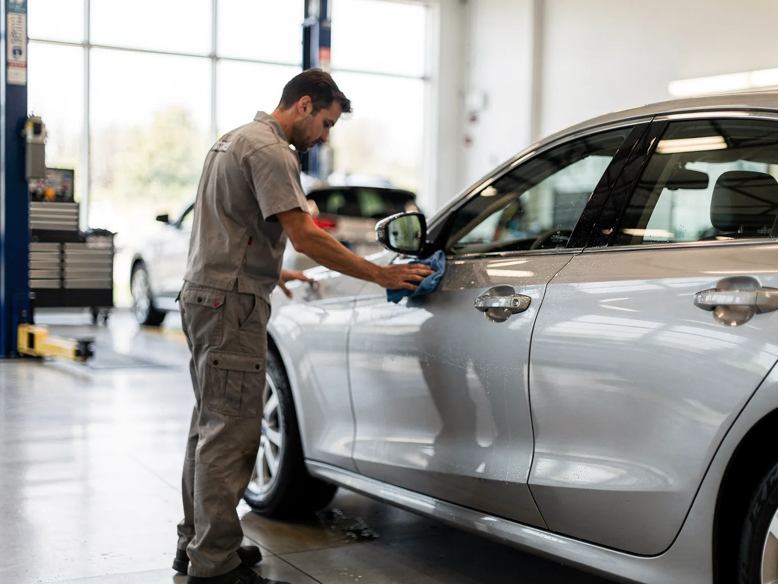 Detailer wiping down a certified pre-owned sedan inside a bright dealership service bay