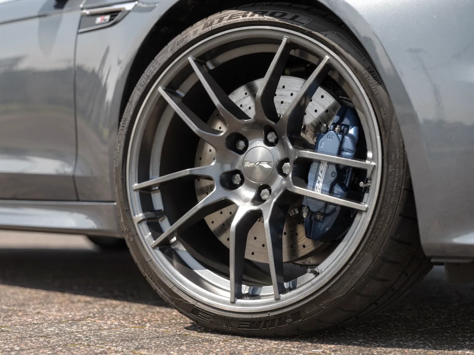 Close-up of a sport sedan front wheel showing a four-piston fixed brake caliper behind an 18-inch alloy