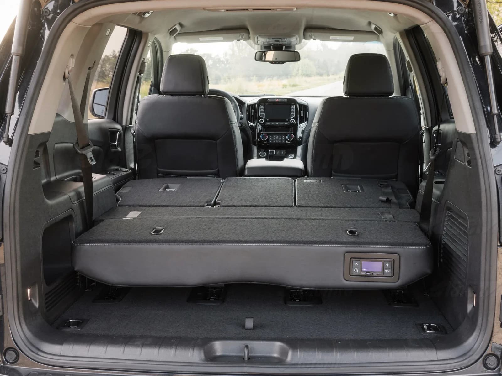 Interior of a full-size SUV showing the second-row bench folded flat and a trailer brake controller on the lower dash