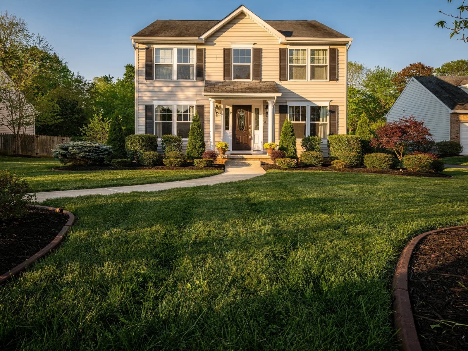 Deep green well-established lawn framed by mulched beds and trimmed shrubs on a two-story home