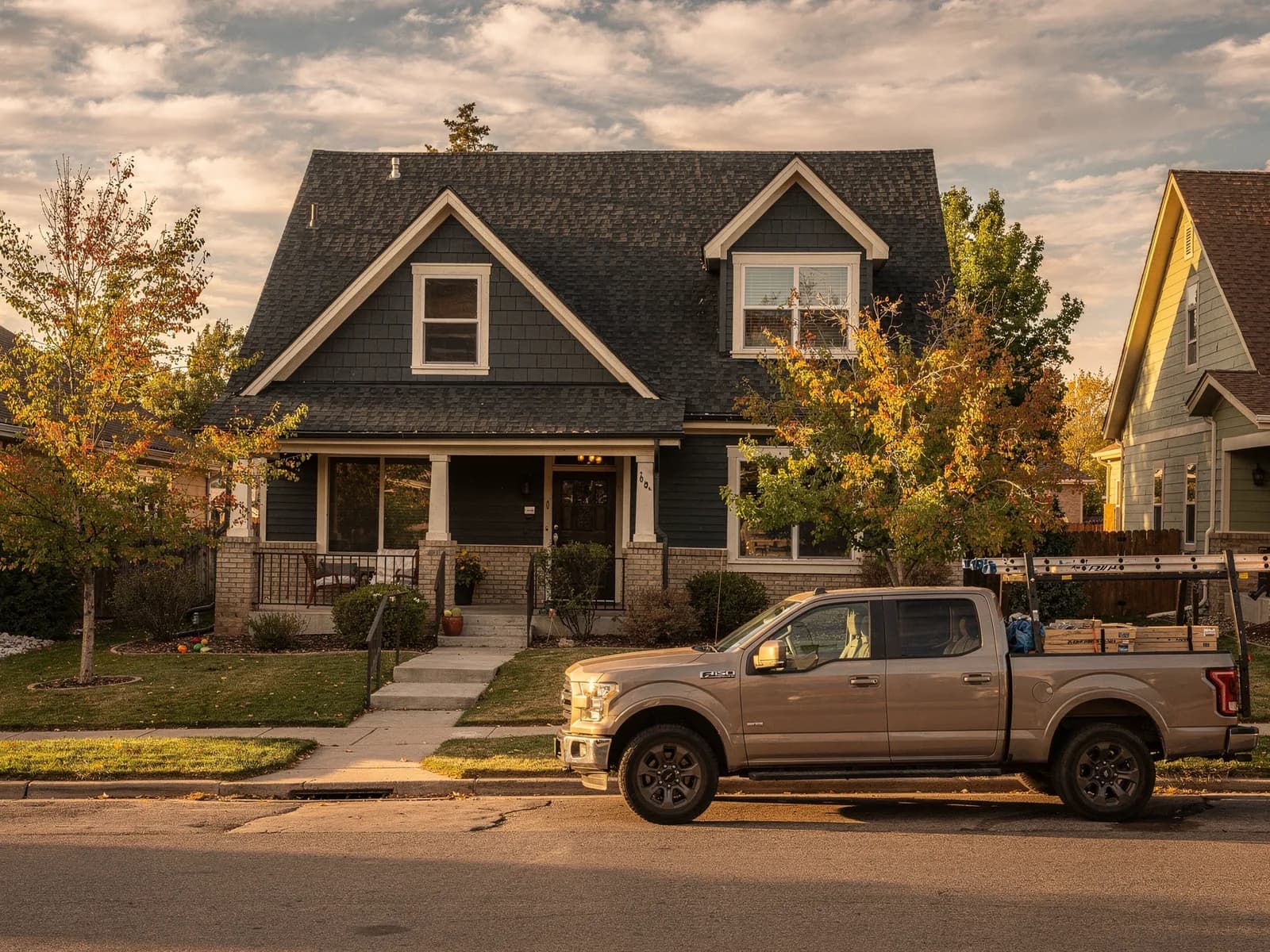 Two-story Denver home with a new charcoal architectural shingle roof, late afternoon light, crew truck parked at the curb