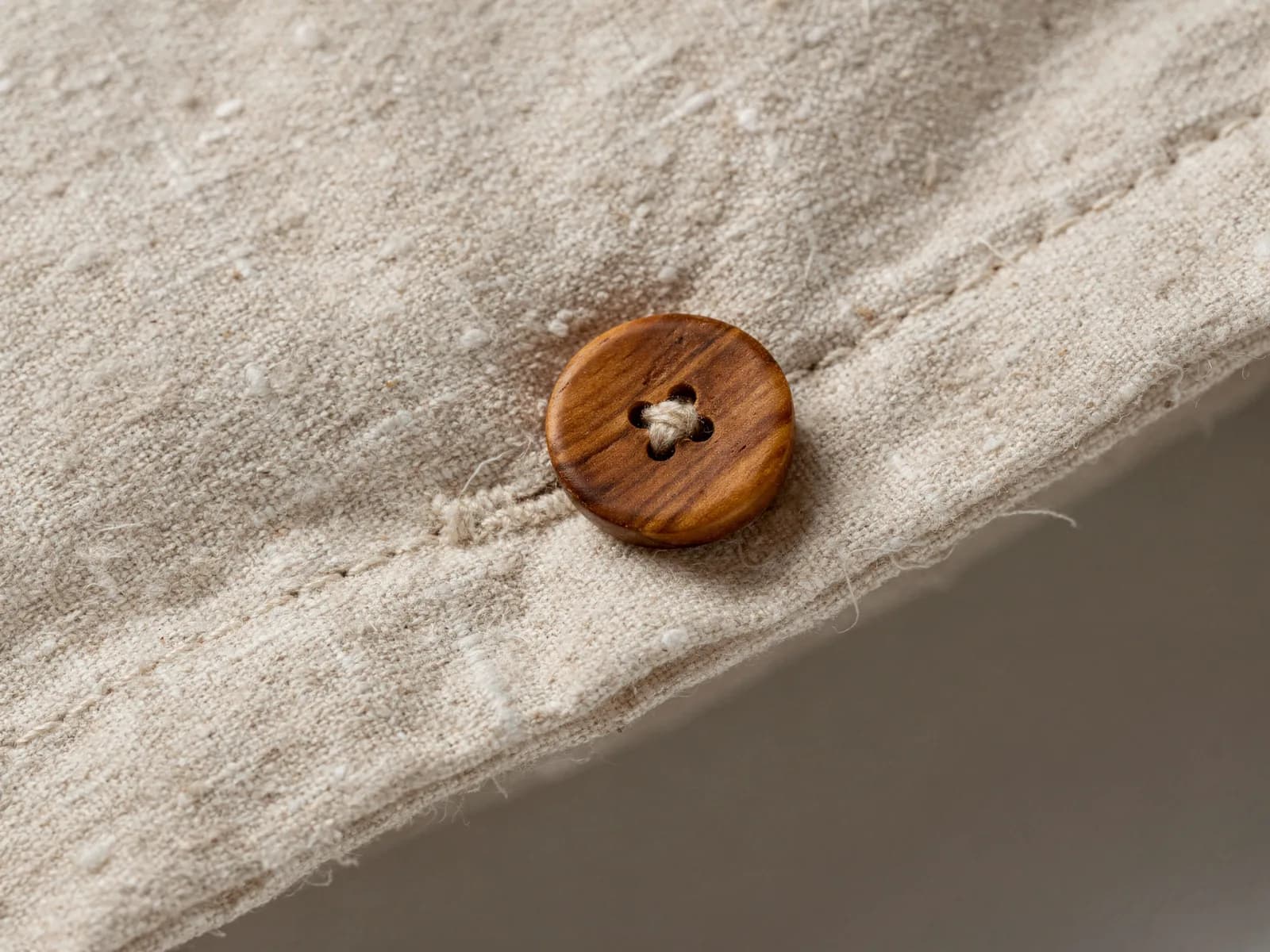 Close-up of a linen duvet cover edge showing a corozo nut button and the visible slub of the flax weave